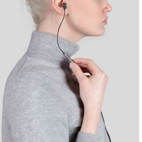Model wearing RHA MA650i Lightning Headphones with Microphone in ear, holding cable, styled with grey roll-neck jumper