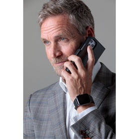 Model with DBramante Lynge iPhone 12/12 Pro 6.1 Inch 2-In-1 Case in black, held to ear, styled with grey check suit and smart watch