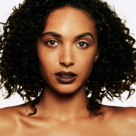 Model wearing MAC Studio Fix Sculpt and Shape Contour Palette in Medium Dark/Dark, with defined contour and deep berry-toned lips