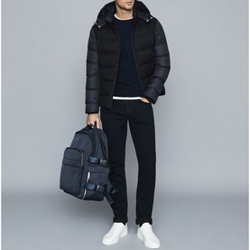 Model wearing Reiss Meyrim Padded Jacket in blue with black trousers and white trainers, carrying a navy backpack