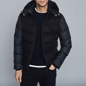 Model wearing Reiss Meyrim Padded Jacket in blue, hooded puffer style, styled with dark jeans and navy crew-neck jumper