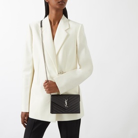 Model carrying Saint Laurent Embossed Leather Envelope Chain Wallet in black with silver hardware, worn crossbody, styled with white blazer