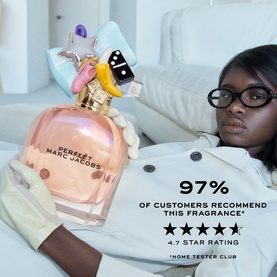Model with Marc Jacobs Perfect Eau de Parfum, large pink bottle with star charm cap, reclining on white sofa