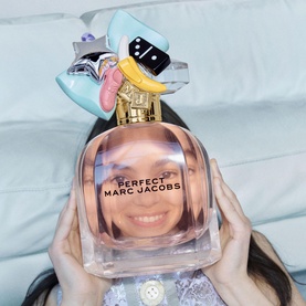 Marc Jacobs Perfect Eau de Parfum held up by a model, showing the rose-gold bottle with whimsical multicoloured cap detail
