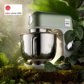Kenwood kMix stand mixer in sage green with polished silver bowl, shown in a lush botanical setting. Red Dot Award winner 2020.