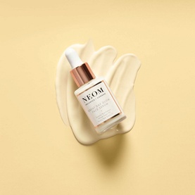 Neom Organics Great Day Glow Face Serum 28ml in white, pump bottle with rose gold cap shown with cream texture swatch on yellow background