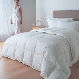 Nimbus Quilt Goose Down 10.5 Tog Duvet Bronze Collection in white, shown on a made bed with model standing beside in bright room