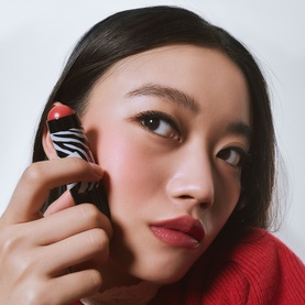 Model with Sisley Phyto-Blush Twist blush compact held to cheek, zebra-print and red packaging, styled with red knitwear