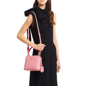 Model carrying Prada Accessories Matin&eacute;e Saffiano Leather Micro Bag in pink with gold-tone triangle logo, worn crossbody over black dress