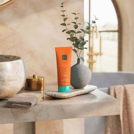 Rituals The Ritual of Karma After Sun Hydrating Lotion orange tube on marble shelf, styled with ceramic vase and eucalyptus stems