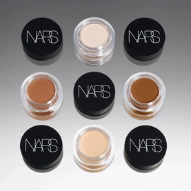 NARS Soft Matte Complete Concealer in Cacao, shown alongside six open pots displaying a range of concealer shades from light to deep