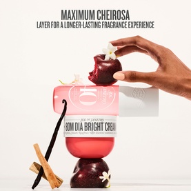 Sol De Janeiro Bom Dia Bright Body Cream jar styled with cherries, vanilla, and cinnamon in a fragrance layering lifestyle shot.