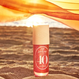 Sol De Janeiro Cheirosa '40 Hair + Body Fragrance Mist in red bottle, placed on sandy beach with warm golden backdrop