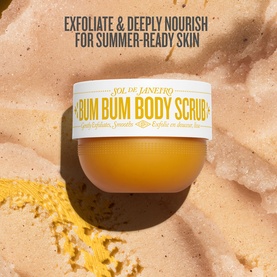 Sol De Janeiro Bum Bum Body Scrub in open white jar, surrounded by golden sandy scrub texture with exfoliating granules visible