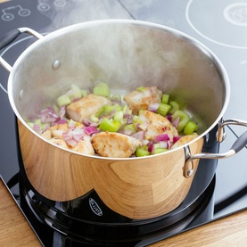 Stellar James Martin Casserole Pan 24cm in stainless steel on induction hob, cooking chicken with diced vegetables, steam rising