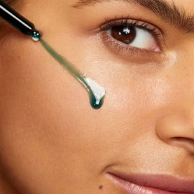Sunday Riley Luna Sleeping Night Oil shown as a green dropper applying a drop of oil to a model's cheek