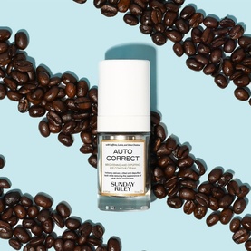 Sunday Riley Auto Correct eye contour cream in glass bottle with white cap, surrounded by coffee beans on a light blue background.