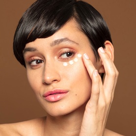 Model with Sunday Riley Auto Correct eye cream, shown dotted under eye area, fingers gently pressing product into skin