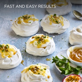 White meringues topped with passionfruit curd and herbs on a grey surface, styled with a bowl of curd and fresh passionfruit