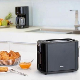 Braun PurEase 2 Slice Toaster in black on kitchen counter, styled with croissants, jam, and a coffee maker in the background