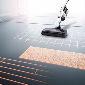 Miele Triflex HX1 Cordless Vacuum Cleaner in white, shown cleaning hard floor transitioning onto carpet with orange light guide effect