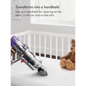 Dyson Home V10 Cyclone Absolute Cordless Stick Vacuum Cleaner in handheld mode, shown upright in a nursery cot setting with a teddy bear