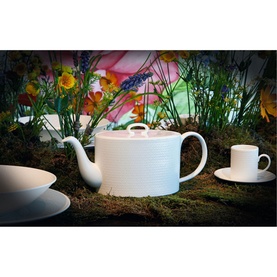 Wedgwood Gio Teapot in white fine bone china with embossed geometric pattern, styled with matching cup and saucer on moss with floral backdrop