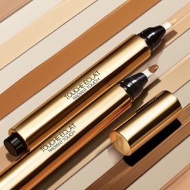 Yves Saint Laurent Touche Eclat concealer pens in gold packaging, shown open and closed against a striped nude tone background
