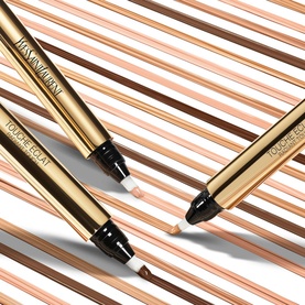 Yves Saint Laurent Touche Eclat concealer pens in gold packaging, shown open and closed on a striped gold background
