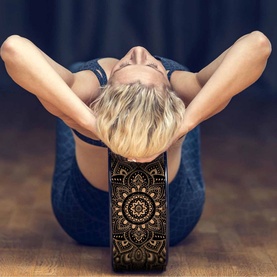 Yoga Design Lab Mandala Yoga Wheel in use, featuring gold mandala print on black, supporting model in a deep forward fold stretch