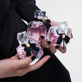 Yves Saint Laurent Mon Paris Eau de Toilette collection of three pink glass bottles with crystal tops and black ribbon bows, held in hands