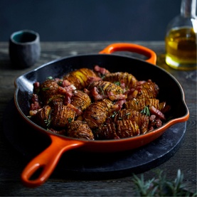 Le Creuset Signature Cast Iron Frying Pan 26cm in orange, filled with hasselback potatoes and bacon, styled on a dark wooden surface