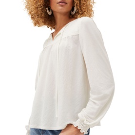Model wearing Phase Eight Viviana Tie Neck Jersey Blouse in cream with long sleeves, frill cuffs, and tie neckline, styled with blue jeans