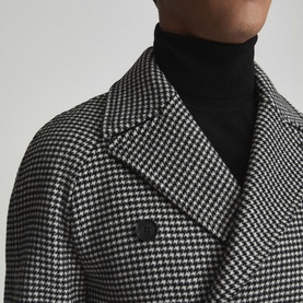 Model wearing Reiss General Houndstooth Double-Breasted Coat in black, showing notch lapels and houndstooth pattern, styled with black roll-neck