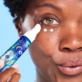 Model with Sunday Riley Retinoid + Niacinamide Eye Serum applied as two dots under the eye, held in a blue illustrated bottle