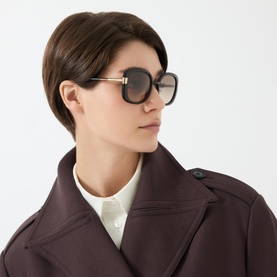 Model with Prada Rectangle Sunglasses 0PR 04WS in brown, oversized square frames with gold-tone hardware, styled with dark coat