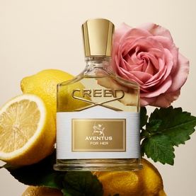 Creed Aventus For Her Eau de Parfum in gold-capped glass flacon, styled with fresh lemons and a pink rose