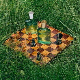 Creed Original Vetiver Eau de Parfum green glass bottles displayed on a wooden chessboard set in long grass