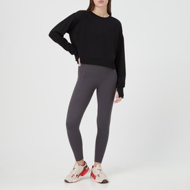 Model wearing Sweaty Betty After Class Cropped Sweatshirt in black, styled with dark grey leggings and white and red trainers