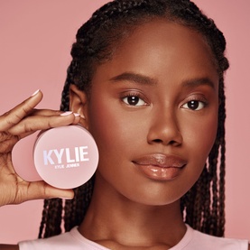 Model with Kylie by Kylie Jenner Setting Powder 10g compact, held up beside face against pink background