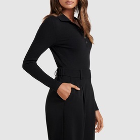Model wearing Forever New Julia Long Sleeve Polo Top in black, with fitted sleeves and polo collar, styled with black wide-leg trousers