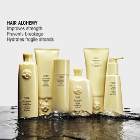 Oribe Hair Alchemy collection displayed on wet surface, featuring serum, shampoo, conditioner and styling products in gold packaging