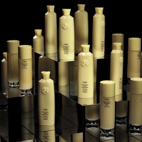 Oribe Hair Alchemy Fortifying Serum displayed alongside multiple Oribe haircare products in cream packaging on a reflective surface