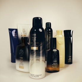 Oribe Hair Alchemy Fortifying Serum shown alongside a collection of Oribe haircare products in dark navy and gold packaging