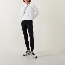 Model wearing Sweaty Betty After Class Cropped Sweatshirt in white, styled with black leggings and multicolour trainers