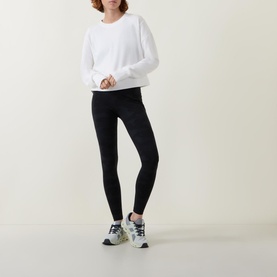 Model wearing Sweaty Betty After Class Cropped Sweatshirt in white, styled with black leggings and grey trainers