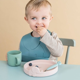 Done By Deer Two-Pack Peekaboo Elphee Bibs in blue silicone, worn by a toddler eating at a table with matching cup and plate