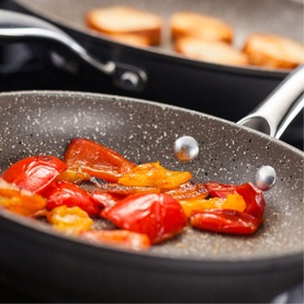 Stellar Rocktanium Non-Stick Two-Piece Frying Pan Set in grey, saut&eacute;ing red and yellow peppers, with riveted stainless steel handles visible