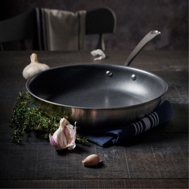 Stellar Eclipse Non-Stick Frying Pan 28cm in stainless steel with long handle, styled on dark wood surface with garlic and herbs