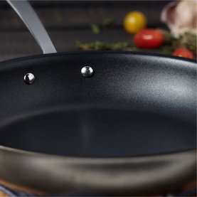 Stellar Eclipse Non-Stick Frying Pan 28cm in dark non-stick interior with stainless steel rivets, tomatoes and garlic visible in background